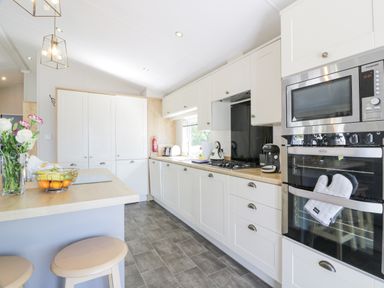 A kitchen with white cabinets a wooden countertop a built-in oven and microwave and stools at Bethany's Retreat in Wemyss Bay