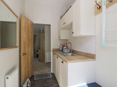 A kitchen with white cabinets a wooden countertop a sink and an open door leading to another room at Bethany's Retreat in Wemyss Bay