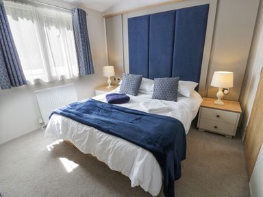 A bedroom with a double bed blue headboard two bedside tables with lamps and patterned blue curtains at Bethany's Retreat in Wemyss Bay