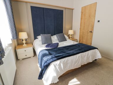 A bedroom with a double bed blue headboard bedside tables with lamps patterned curtains and a wooden door at Bethany's Retreat in Wemyss Bay