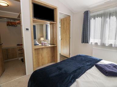 A bedroom with a bed and a navy blanket next to a window with curtains at Bethany's Retreat in Wemyss Bay
