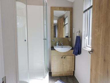 A bathroom with a corner shower cubicle a wooden vanity unit with a sink and mirror and a window with blinds at Bethany's Retreat in Wemyss Bay