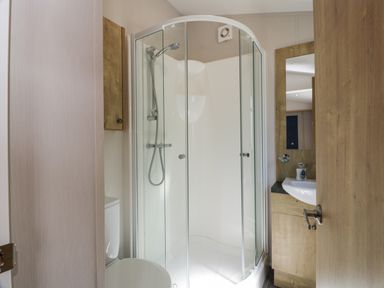 A bathroom with a curved glass shower enclosure a toilet and a sink with a mirror at Bethany's Retreat in Wemyss Bay