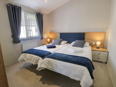 A bedroom with two single beds with blue throws and pillows two bedside tables with lamps and a window with blue curtains at Bethany's Retreat in Wemyss Bay
