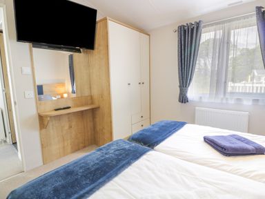 A bedroom with twin beds blue blankets and towels a wall mounted television and a wardrobe at Bethany's Retreat in Wemyss Bay