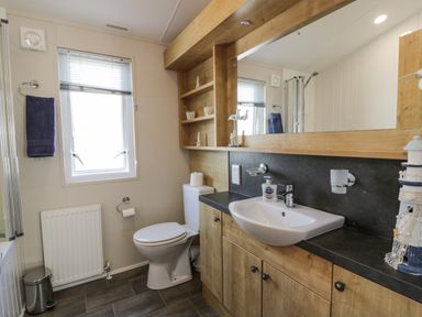 A bathroom with a toilet sink mirror wooden cabinets and a window at Bethany's Retreat in Wemyss Bay