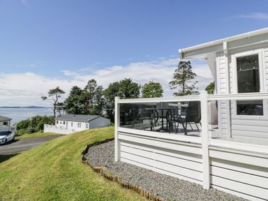 A patio with chairs and a table next to a white building on a grassy hill overlooking water at Bethany's Retreat in Wemyss Bay
