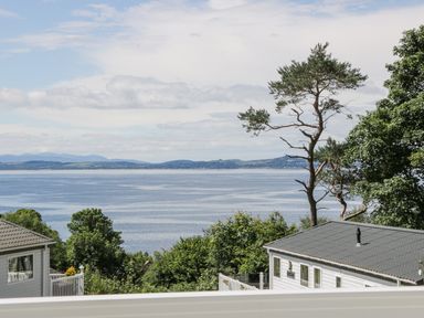 A view of a body of water with trees and houses in the foreground and hills in the distance at Bethany's Retreat in Wemyss Bay