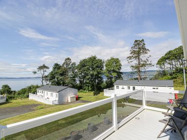A balcony with chairs overlooking white buildings green trees and a body of water at Bethany's Retreat in Wemyss Bay