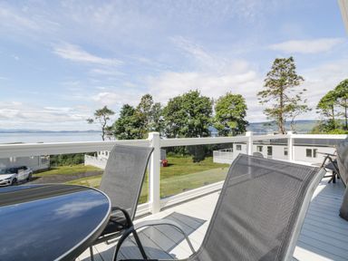 An outdoor deck with a round glass table and two mesh chairs overlooking trees and mobile homes at Bethanys Retreat in Wemyss Bay