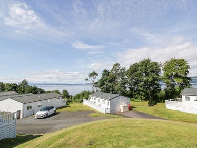 A view of several white mobile homes with parked cars surrounded by grass and trees overlooking a body of water at Bethany's Retreat in Wemyss Bay