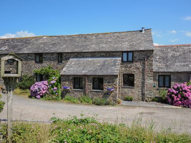 A stone house with multiple windows flowers and plants along the front and a clear sky at West Lee in Bude