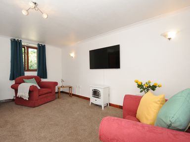 A living room with two red armchairs a wall mounted television and yellow flowers at West Lee in Bude