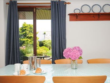 A dining table with a polka dot tablecloth cups croissants and a vase of flowers near a window with blue curtains at West Lee in Bude