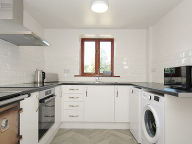 A kitchen with white cabinets black countertops a window sink oven washing machine and microwave at West Lee in Bude