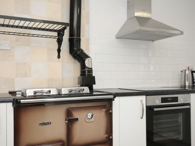A kitchen with a brown Aga stove a black extractor hood a stainless steel oven a kettle and white cupboards at West Lee in Bude