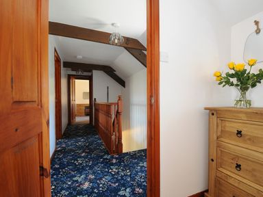 A hallway with blue floral carpet wooden doors and beams and a wooden chest with yellow flowers at West Lee in Bude