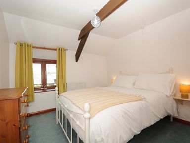 A bedroom with a white metal bed frame a wooden chest of drawers and a window with yellow curtains at West Lee in Bude