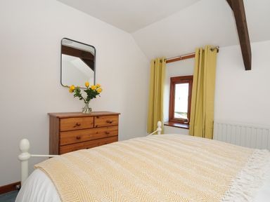 A bedroom with a wooden dresser and yellow flowers under a mirror beside a window with yellow curtains at West Lee in Bude