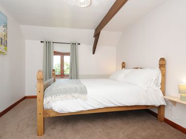 A bedroom with a wooden bed a window with curtains and a wall shelf with a lamp at West Lee in Bude