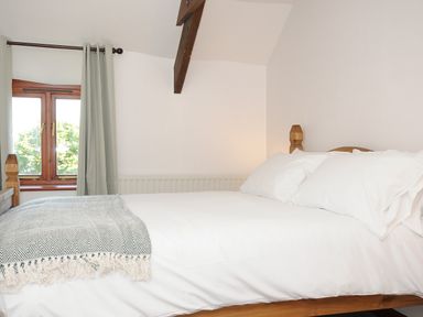 A bedroom with a wooden bed white bedding a window with light curtains and a wooden beam on the ceiling at West Lee in Bude