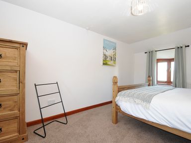 A bedroom with a wooden bed and chest of drawers a metal towel rack and a window with curtains at West Lee in Bude