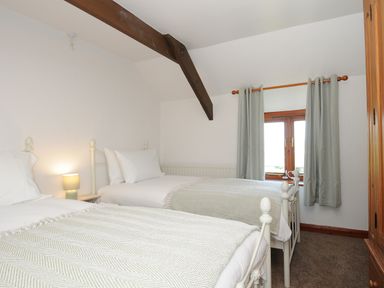 A bedroom with two single beds side by side under a wooden beam with a window and curtains at West Lee in Bude
