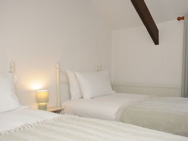 A bedroom with two single beds a nightstand with a lamp and a wooden ceiling beam at West Lee in Bude