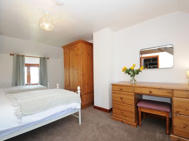 A bedroom with two single beds a wooden wardrobe a wooden dresser a mirror and a vase with yellow flowers at West Lee in Bude