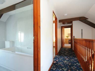 A hallway with wooden railing and floral carpet leading to rooms including a bathroom and bedroom at West Lee in Bude