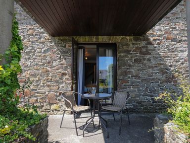 A stone wall with a glass door leading to a patio with a round table and two wicker chairs at West Lee in Bude