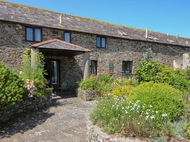 Stone exterior of a house with a covered porch and garden beds with flowers and shrubs at West Lee in Bude