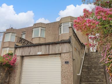 A house with bay windows a garage door and a concrete staircase with pink flowering plants at Small Hillman in Perranporth