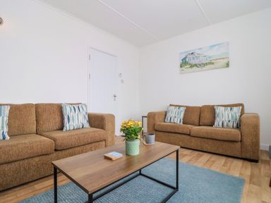 A living room with two brown sofas, a wooden coffee table, a potted plant, and a wall painting at Small Hillman in Perranporth