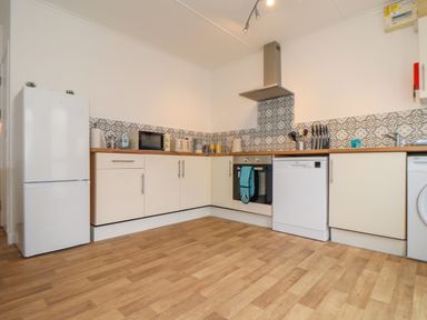 A kitchen with white cabinets wooden countertops patterned tile backsplash and various appliances including fridge microwave oven dishwasher and washing machine at Small Hillman in Perranporth