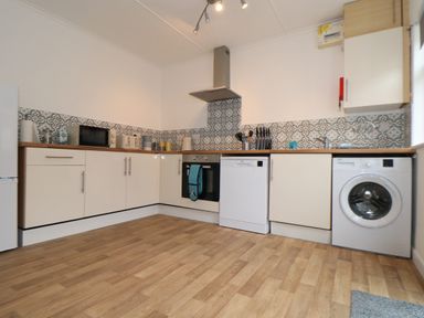 A kitchen with white cabinets wooden countertops patterned backsplash and appliances at Small Hillman in Perranporth