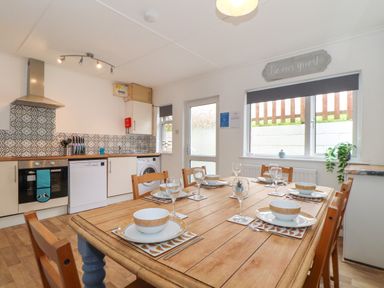 A kitchen with a wooden dining table set for six with kitchen appliances and patterned tile backsplash at Small Hillman in Perranporth