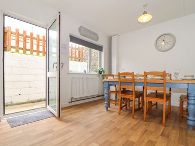 A dining room with wooden chairs and a blue table and an open door leading outside at Small Hillman in Perranporth
