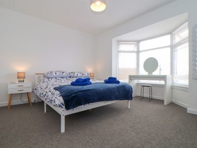 A bedroom with a bed with patterned bedding and folded towels bedside tables with lamps and a desk with a round mirror at Small Hillman in Perranporth