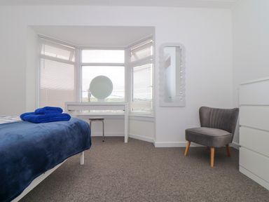 A bedroom with a bed with towels on it a dressing table with a mirror a stool a grey chair and a chest of drawers at Small Hillman in Perranporth