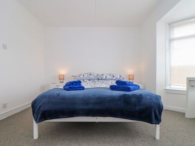 A bedroom with a double bed blue blankets and pillows and two bedside tables with lamps at Small Hillman in Perranporth