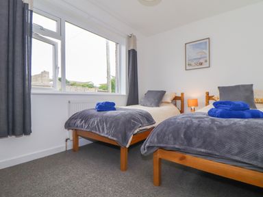A bedroom with two single wooden beds grey blankets blue towels on beds a window and a framed picture on the wall at Small Hillman in Perranporth