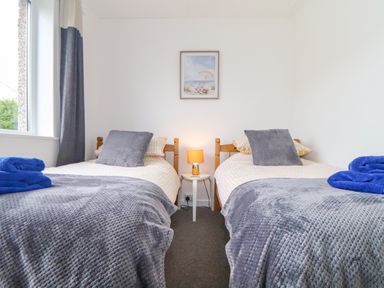 A bedroom with two single beds with gray blankets and blue towels at Small Hillman in Perranporth