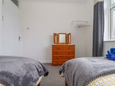 A bedroom with two single beds gray blankets wooden dresser with a three-panel mirror and a clothes rack with hangers at Small Hillman in Perranporth