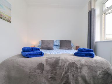 A bed with patterned bedding and two gray pillows with blue towels on a gray blanket in a bedroom at Small Hillman in Perranporth