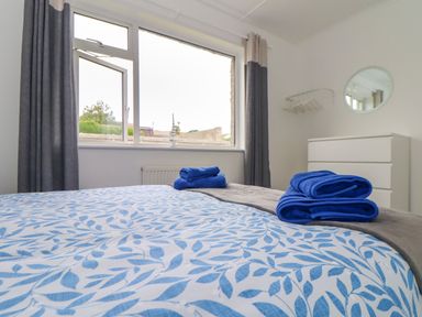 A bedroom with a window curtains dresser mirror and folded blue towels on a bed at Small Hillman in Perranporth