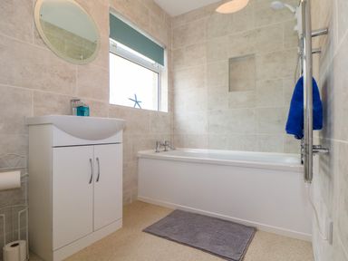 A bathroom with a sink cabinet mirror window bathtub and towel rack at Small Hillman in Perranporth