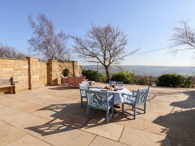 An outdoor patio area with a table and four chairs set for breakfast and stone walls at Roding Cottage in Egton