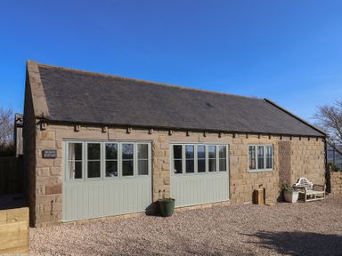 Stone cottage with three sets of windows and two planters on a gravel driveway at Roding Cottage in Egton