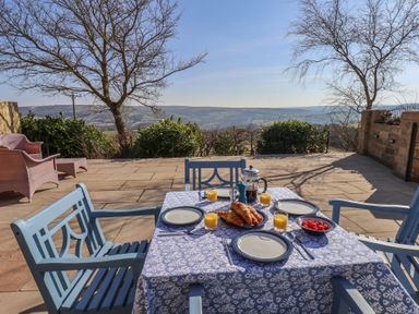 An outdoor patio with a table set for breakfast with plates croissants orange juice and strawberries at Roding Cottage Egton